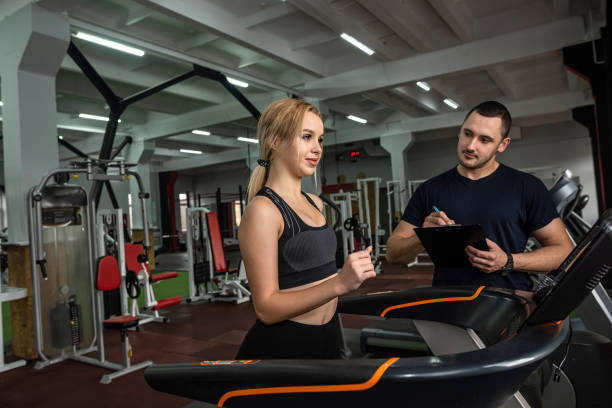 istock Fit female client running on treadmill with her personal trainer in a sport centre 1404419663