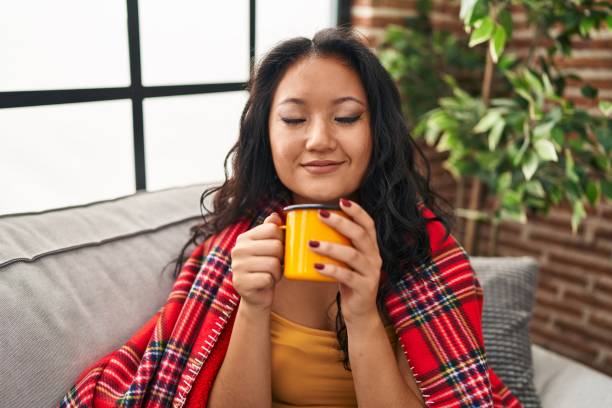 istock Young chinese woman drinking coffee sitting on sofa at home 1404420200