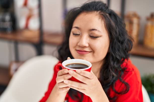 istock Young chinese woman drinking coffee sitting on table at home 1404420496