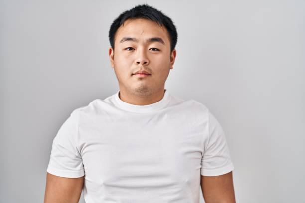 istock Young chinese man standing over white background relaxed with serious expression on face. simple and natural looking at the camera. 1404420687