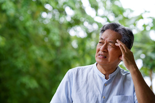 Portrait of an elderly man having a headache while standing in a park