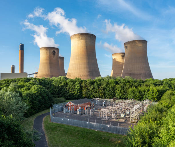 Aerial view of an electricity generating power station with electrical equipment An aerial view of the cooling towers and chimney of a large coal fired power station generating electricity with electrical equipment to supply power to the national Grid via transformers cooling tower photos stock pictures, royalty-free photos & images