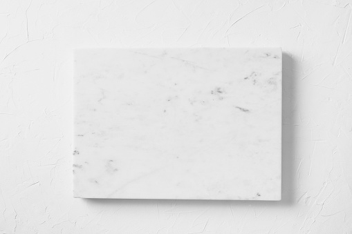 Empty white marble board on light gray stone table. Food and cooking background with free space for text. Cooking concept with copy space. Top view.