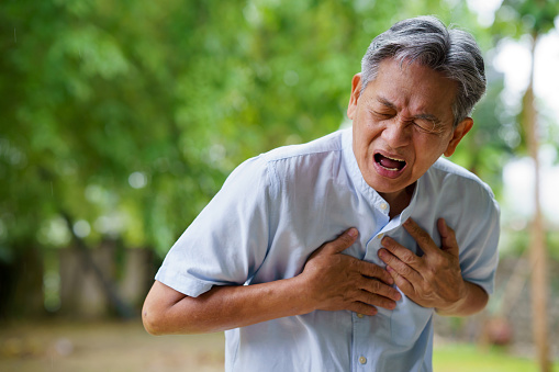 Closeup shot of a senior asian man holding his chest in discomfort outdoors