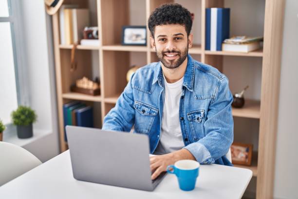 istock Young arab man using laptop drinking coffe sitting on table at home 1404422693