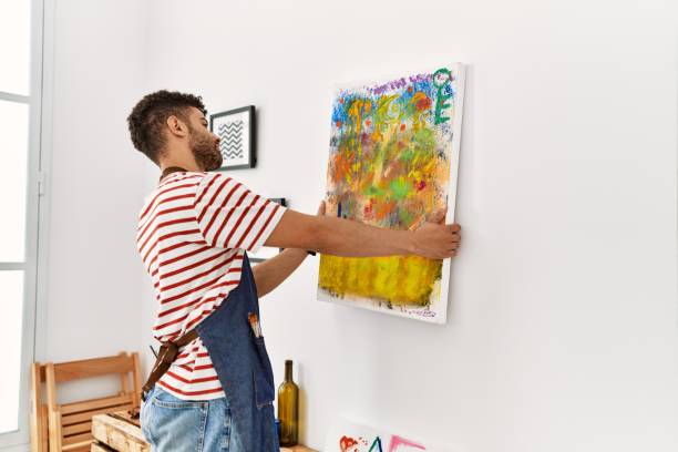 istock Young arab artist man on back view hanging draw canvas on wall at art studio. 1404422912