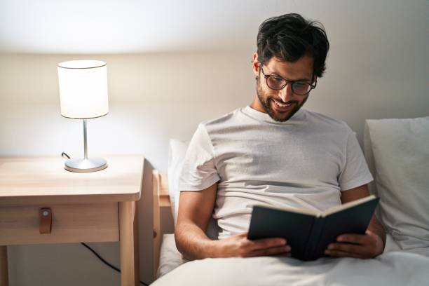 istock Young hispanic man reading book sitting on bed at bedroom 1404423325