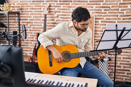 Young hispanic man musician playing classical guitar at music studio