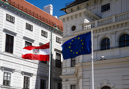 State Flag of Austria and European Union Flag Close-Up, Office of the Federal President of the Republic of Austria Leopoldine Wing of Hofburg Vienna as Historic Former Imperial Palace Complex in the Background, 17th Century Architecture in Late Renaissance Style, in Ballhausplatz Square, Innere Stadt, 1st District of Vienna, Austria, Europe in June 2022