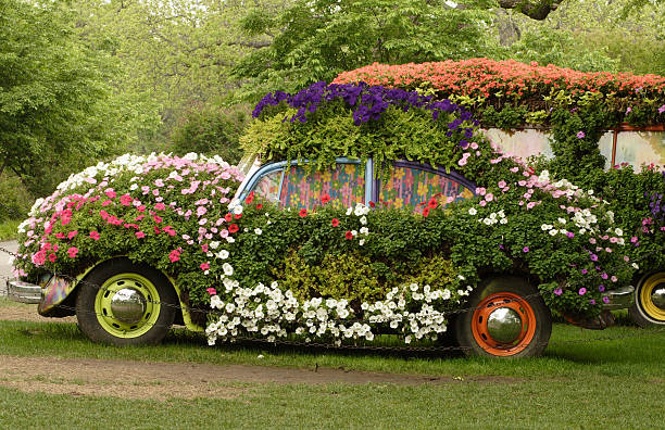 An old yellow car with round headlights and an open hood like a flower bed stands outside a flower shop in the city.