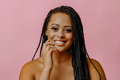 portrait of young adult thoughtful smiling beauty black woman with hand on chin braid hair looking at camera on pink background studio shot