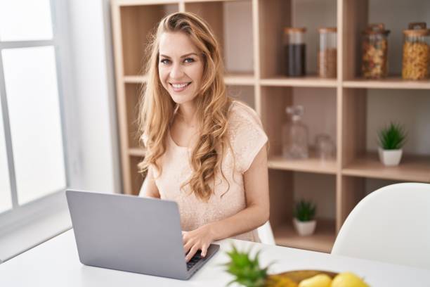 istock Young blonde woman using laptop sitting on table at home 1404434080