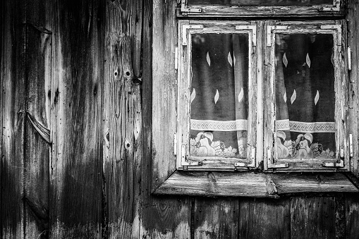 Window with net curtains of very old wooden cottage house, black and white image