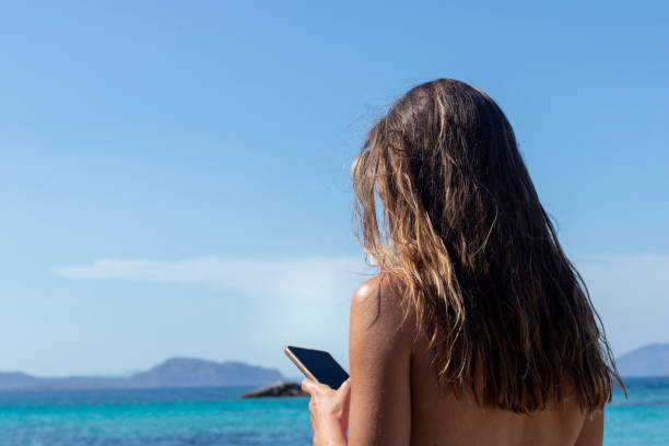 istock Unrecognizable young brunette woman on smartphone while resting at the beach on summer holidays 1404436615