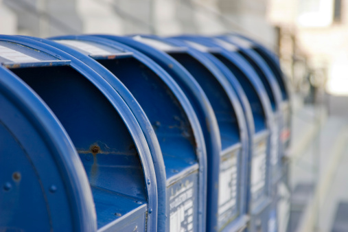 A row of six blue mailboxes on a street in Charleston, South Carolina.  Focus is on the first mailbox's rusty screw head.