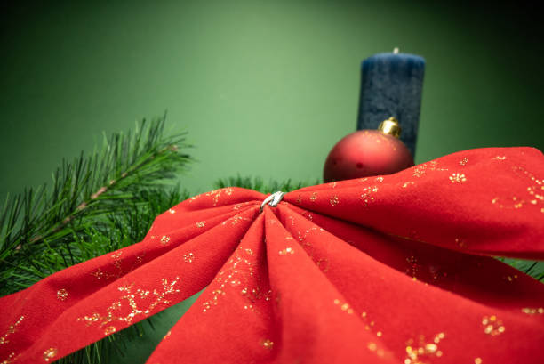 Close-up taken of red paper napkin folded in the shape of Santa Claus Hat on plate with cutlery set and christmas ornaments.