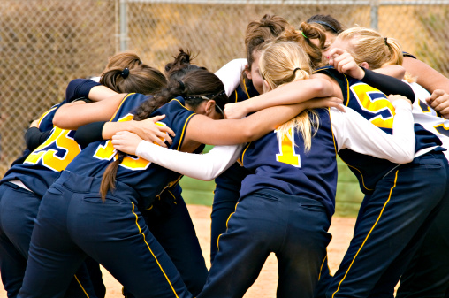 Fastpitch Softball team huddle before the start of a softball game.  Photo is in color.  All logos have been removed.