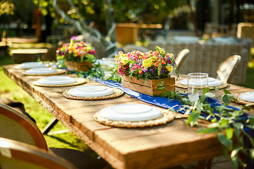 Beautifully decorated wooden table in a summer open-air cafe. Green branch and fresh flowers table decoration