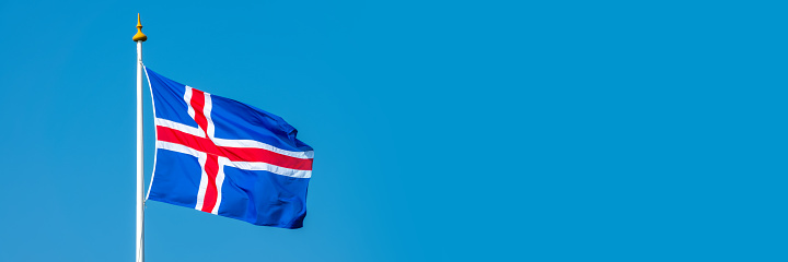 Icelandic flag on a pole floating in the wind on blue sky background, panoramic web banner web banner