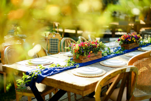 Beautifully decorated wooden table in a summer open-air cafe. Green branch and fresh flowers table decoration