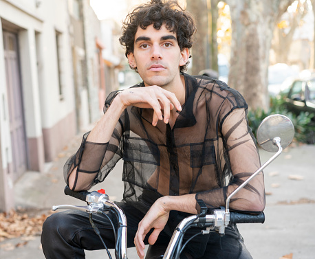 Portrait of a young and confident LGBTQ+ stylish man hanging out in street on a  vintage motorcycle