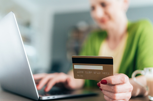 Female hand holding credit card in the foreground. While using laptop for online shopping or online payment. Modern woman shopping online using credit card from home