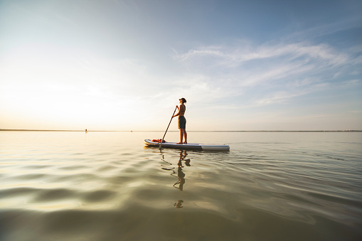 Young woman sup boarding alone at sunset