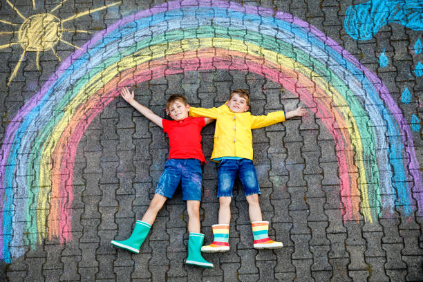 istock Two happy school boys having fun with with rainbow picture drawing with colorful chalks on asphalt. Siblings, twins and best friends painting on ground together. Sign against corona virus. 1404451613