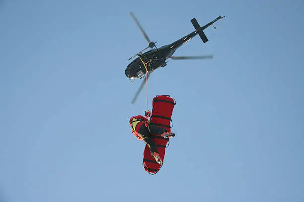 A rescue worker flies undr a helicopter with a patient in a rescue stretcher.