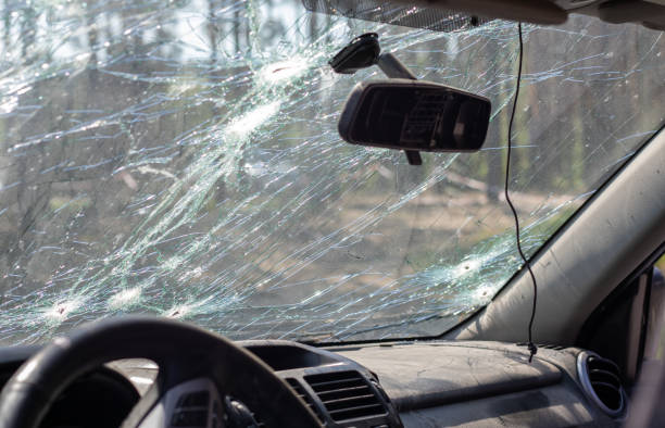 Broken windshield of a car from a bullet, from a shot from a firearm, view from the inside of the cabin. Damaged glass with traces of an oncoming stone on the road. Interior view of the car.