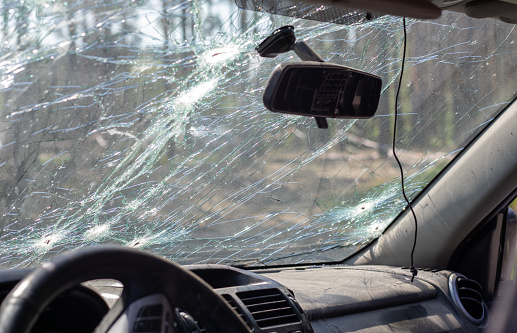 Broken windshield of a car from a bullet, from a shot from a firearm, view from the inside of the cabin. Damaged glass with traces of an oncoming stone on the road. Interior view of the car