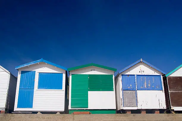 3 beachhuts against a blue sky. Two are pristine, the third is rundown.