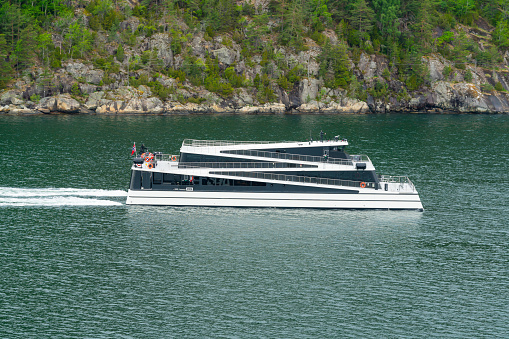 Catamaran Ferry sailing through a narrow sound in the Oslo fjord in Norway with steep rocky coastline in the background.