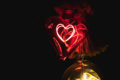Red glass light bulb shaped like a heart glowing in the dark