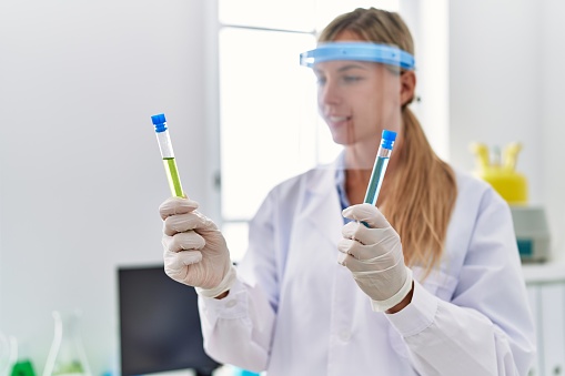 Young blonde woman wearing scientist uniform holding test tubes at laboratory