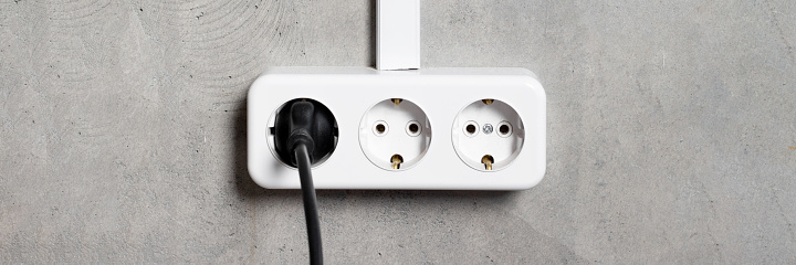 Group of white european electrical outlets with plug on gray concrete wall banner. Wide panoramic header