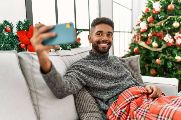 junger afroamerikaner, der selfie am smartphone macht und weihnachten zu hause feiert. - christmas decoration photography themes christmas ornament stock-fotos und bilder