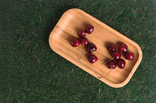 black cherry on wooden plate isolated on green grass background flat lay. Image contains copy space