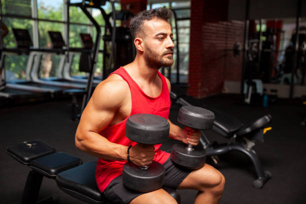 istock Young man having weight training with dumbbells at gym 1404471467