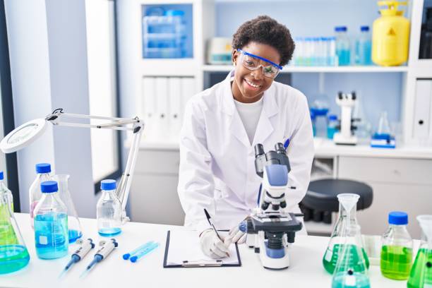 istock African american woman wearing scientist uniform using microscope write on clipboard at laboratory 1404471629