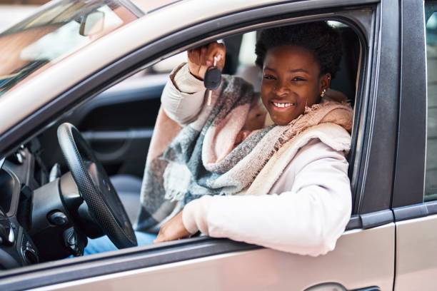 African american woman holding key sitting on car at street stock photo