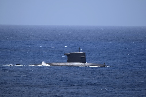 Diesel submarine partially submerged sails by on open water, blue sky on the horizon of the blue ocean