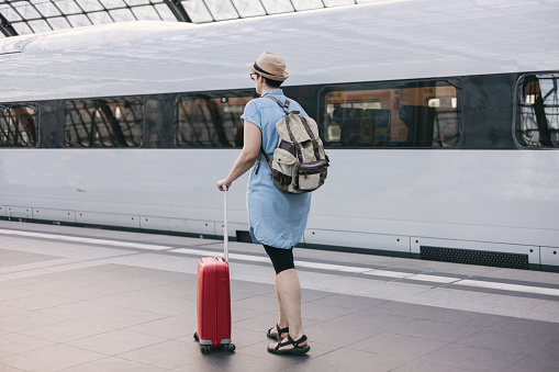 Woman with suitcase waiting for her train on platform of railway station