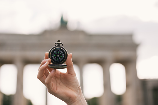 Old classic navigation compass in hand on Brandenburg Gate background, symbol of tourism