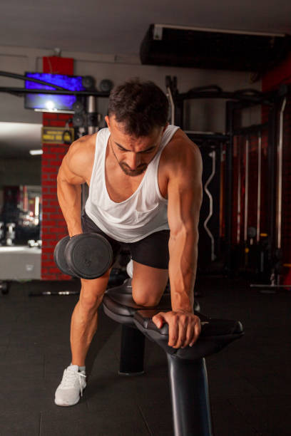 istock Young man having weight training with dumbbells at gym 1404474372