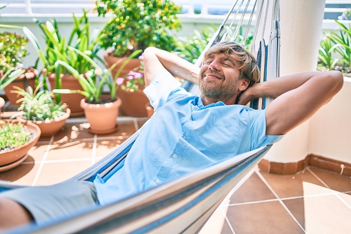 Middle age handsome man at the terrace of his house relaxing lying on a hammock