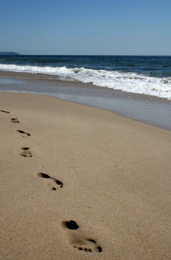 A trail of footprints leading towards the camera with the ocean in the background.
