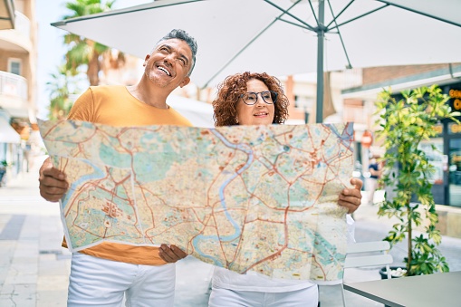 Middle age couple on vacation smiling happy holding map at street of city.