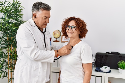 Middle age man and woman wearing doctor uniform auscultate heart having medical consultation at clinic
