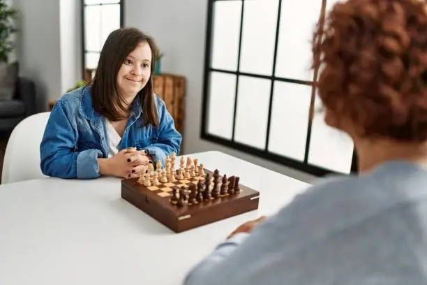 Mature mother and down syndrome daughter playing chess boardgame at home